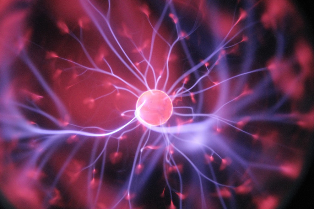 Close-up of a plasma globe with purple and pink electric filaments radiating from the central sphere through ionized gas.