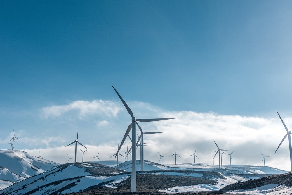 Wind turbines on a snow-covered, hilly landscape under a clear blue sky.