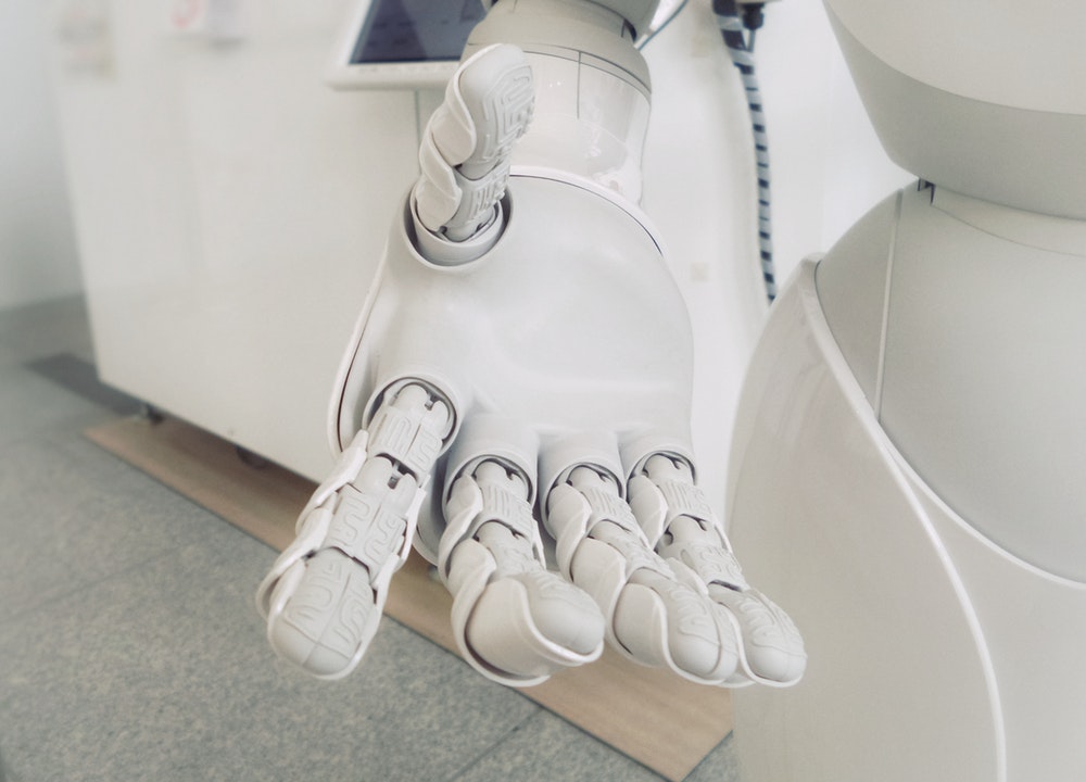 A close-up view of a white humanoid robot's outstretched hand, showing detailed mechanical fingers and joints.