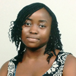 A woman with medium-dark skin and shoulder-length curly hair, wearing a patterned sleeveless top, looks at the camera against a plain background.