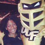 A woman stands next to Knightro, the gold-armored mascot of the University of Central Florida, both smiling for the camera.