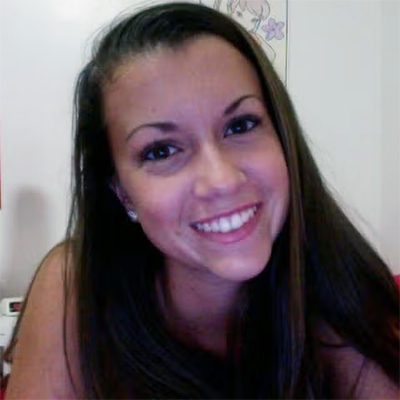 A woman with long dark hair smiles at the camera, seated indoors against a light-colored wall.