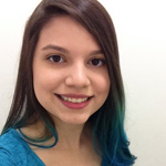 A young woman with straight brown hair and teal tips smiles at the camera, wearing a blue top against a plain white background.