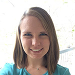 A woman with straight, shoulder-length light brown hair, wearing a turquoise top, smiles at the camera in an outdoor setting.