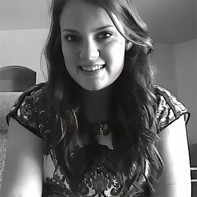 A young woman with long dark hair, wearing a patterned shirt, smiles at the camera in a well-lit indoor setting.