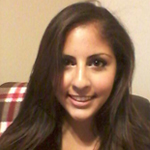 A woman with long dark hair smiles at the camera while sitting indoors. A plaid-patterned blanket is draped on the back of the couch behind her.