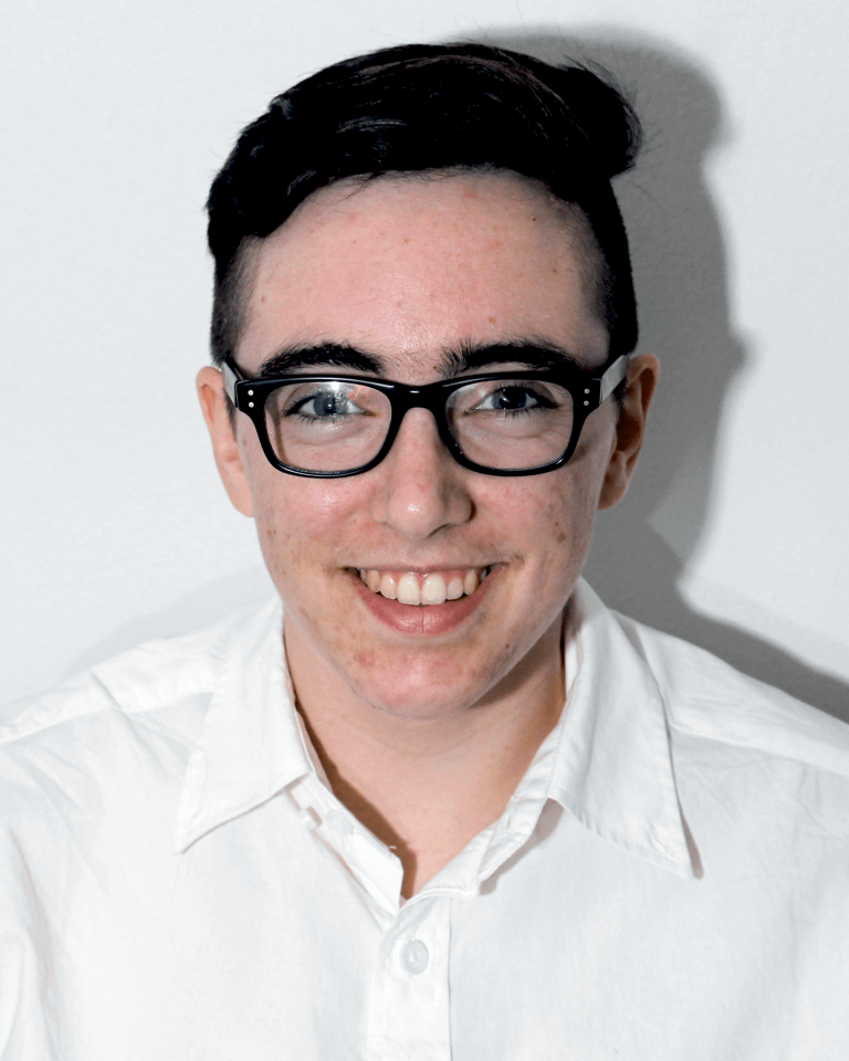 Person with short dark hair, glasses, and a white shirt smiling at the camera against a plain white background.