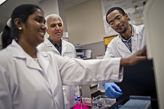 Three scientists in lab coats work together in a laboratory setting, focusing on a scientific instrument.