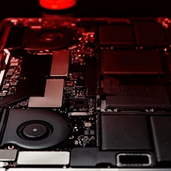 Close-up view of a laptop's internal components, including the cooling fan, circuit boards, and various hardware parts, with a red light illuminating the scene.
