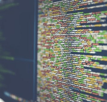A blurred computer screen displays lines of colorful source code in a text editor.
