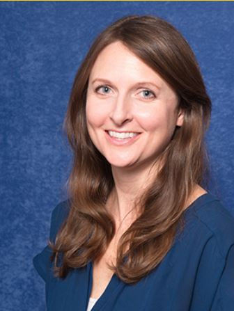 Woman with long brown hair and a blue blouse smiles at the camera in front of a blue textured background.